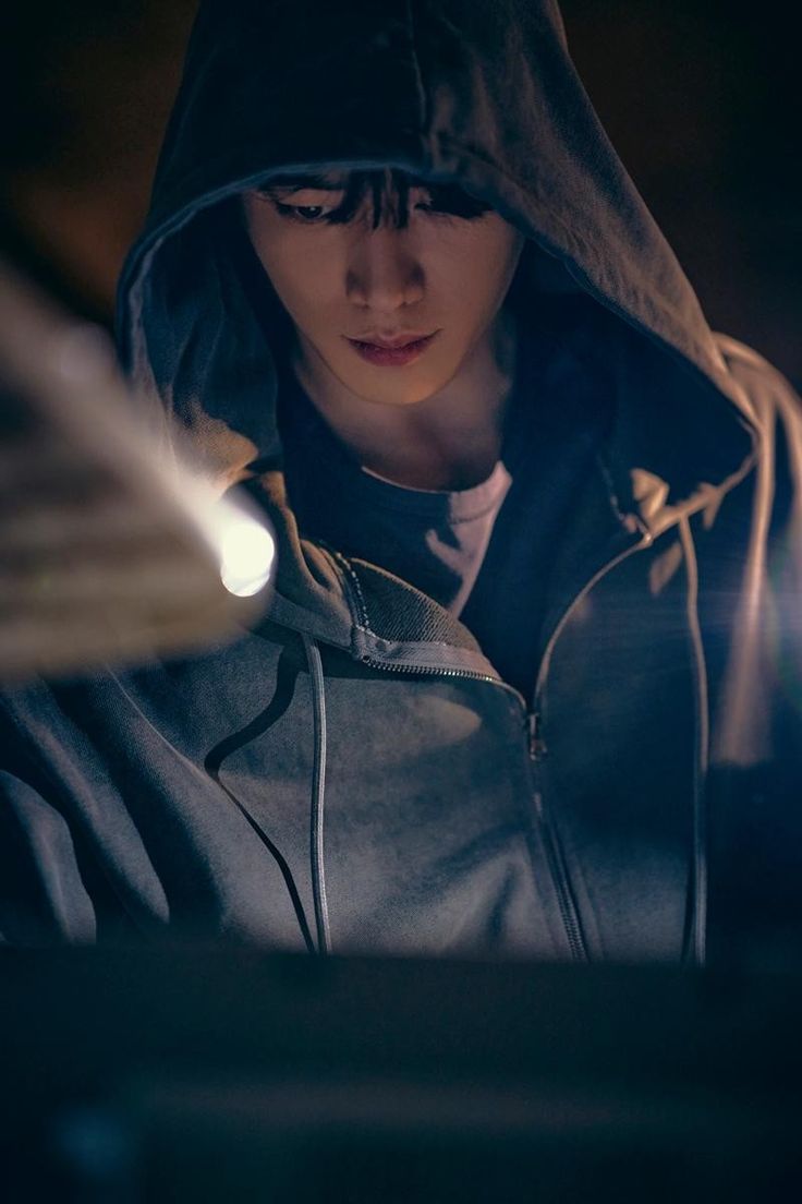 a young man wearing a hoodie looking down at his cell phone in the dark