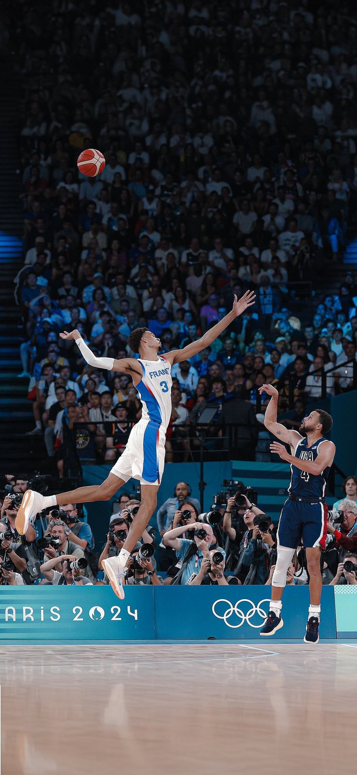 two men are playing basketball in front of a large group of people on the court