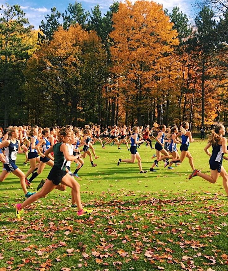 a group of young people running across a lush green field next to trees with leaves on the ground