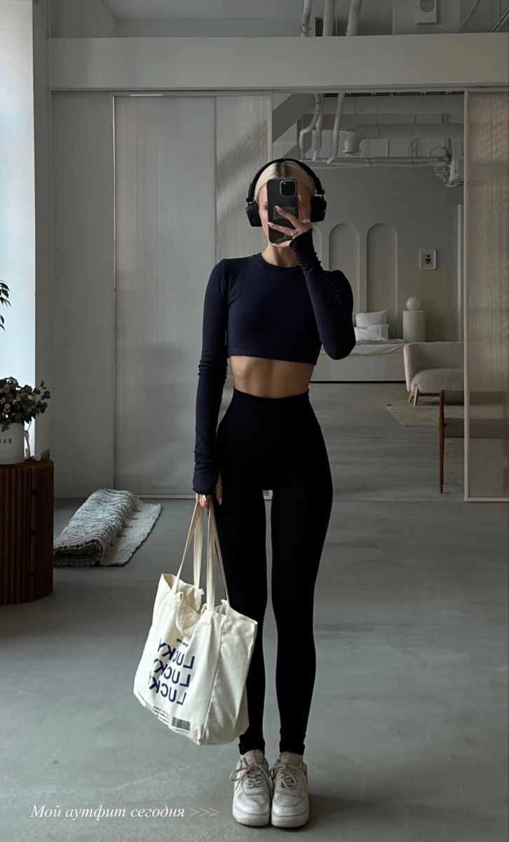 a woman in black top and leggings holding a white bag while talking on a cell phone