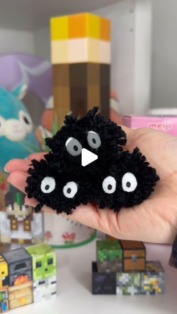 a hand holding a small black object with googly eyes in front of other toys