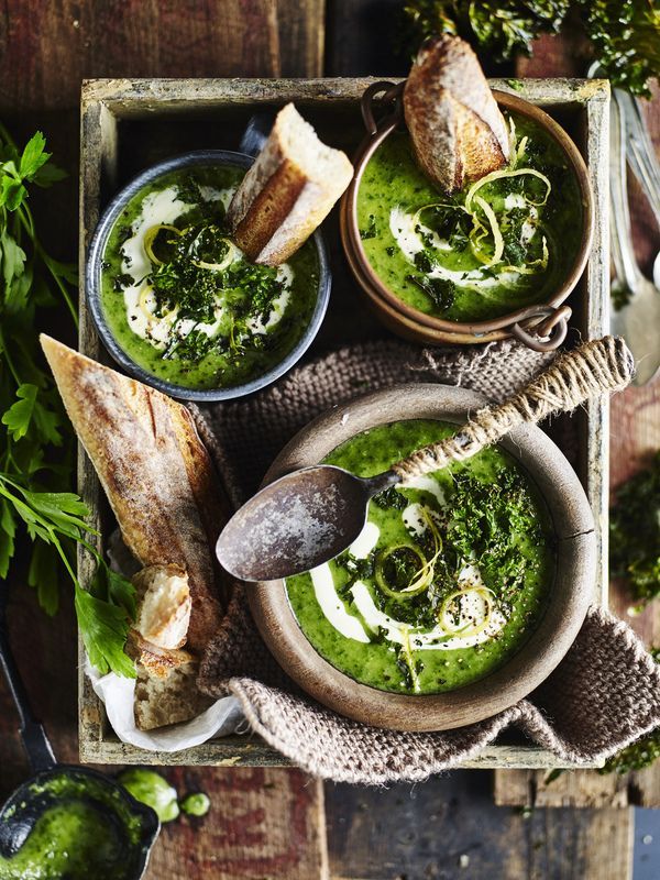 two bowls filled with green soup next to bread