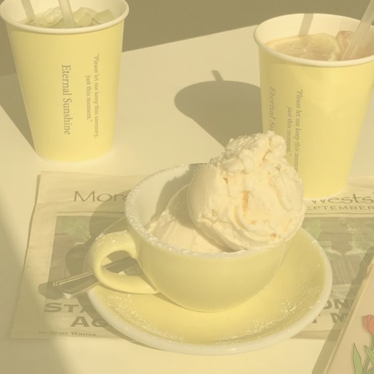 two cups of ice cream sit on a table next to a newspaper and spoons