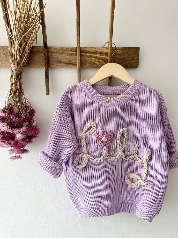 a purple sweater hanging on a wooden hanger next to dried flowers and twigs in the background