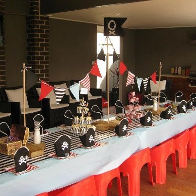 a long table with pirate decorations on it and red chairs in the back drop off area