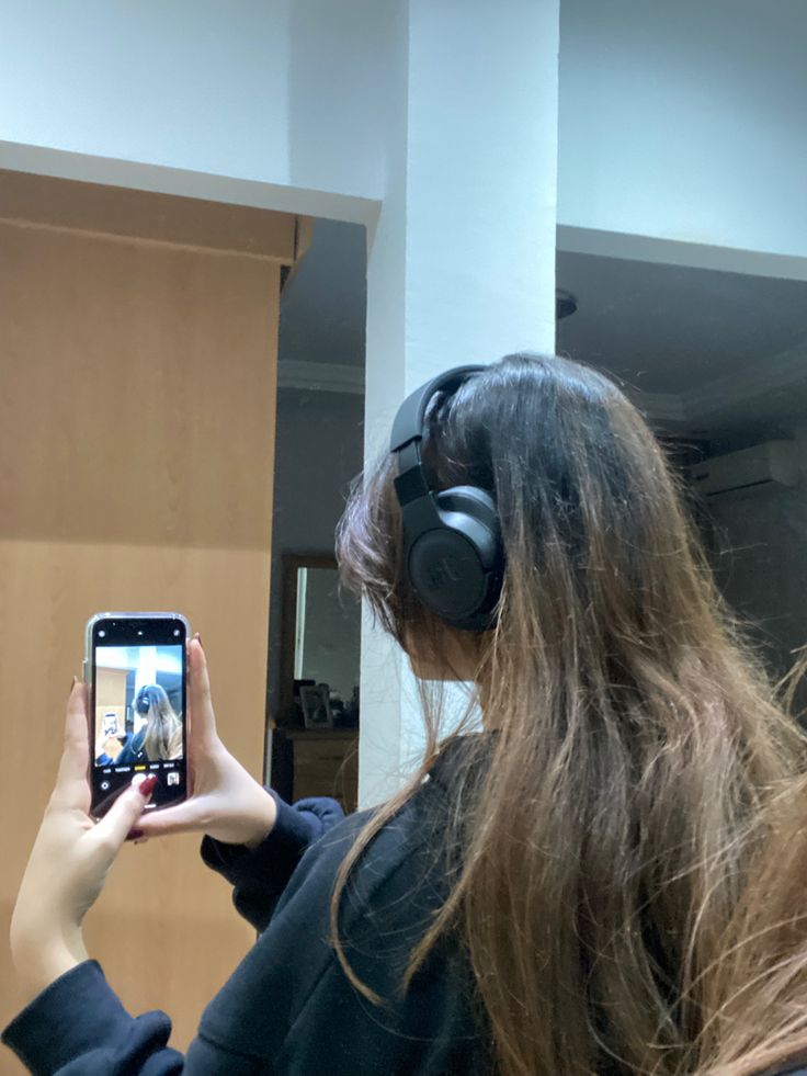 a woman wearing headphones is taking a selfie in front of a mirror with her cell phone