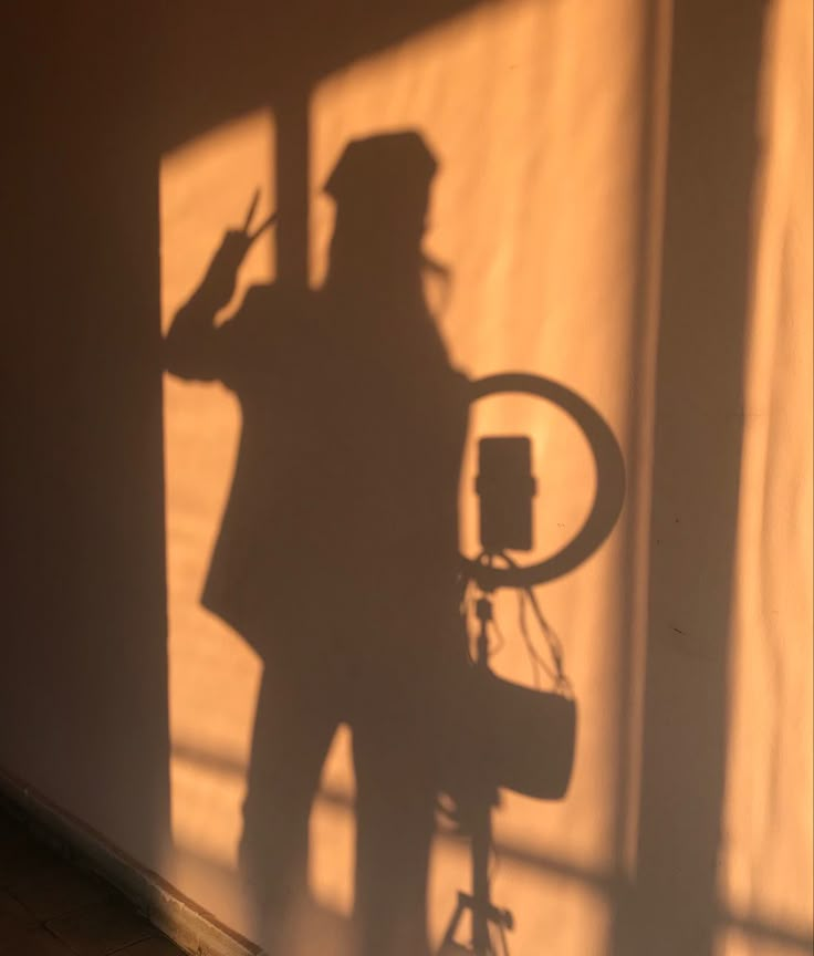 the shadow of a man in a hat and coat holding a camera next to a wall