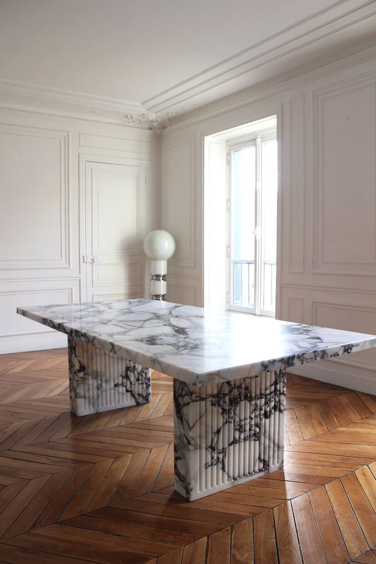 a marble table in an empty room with wood flooring and white walls, along with parquet floors