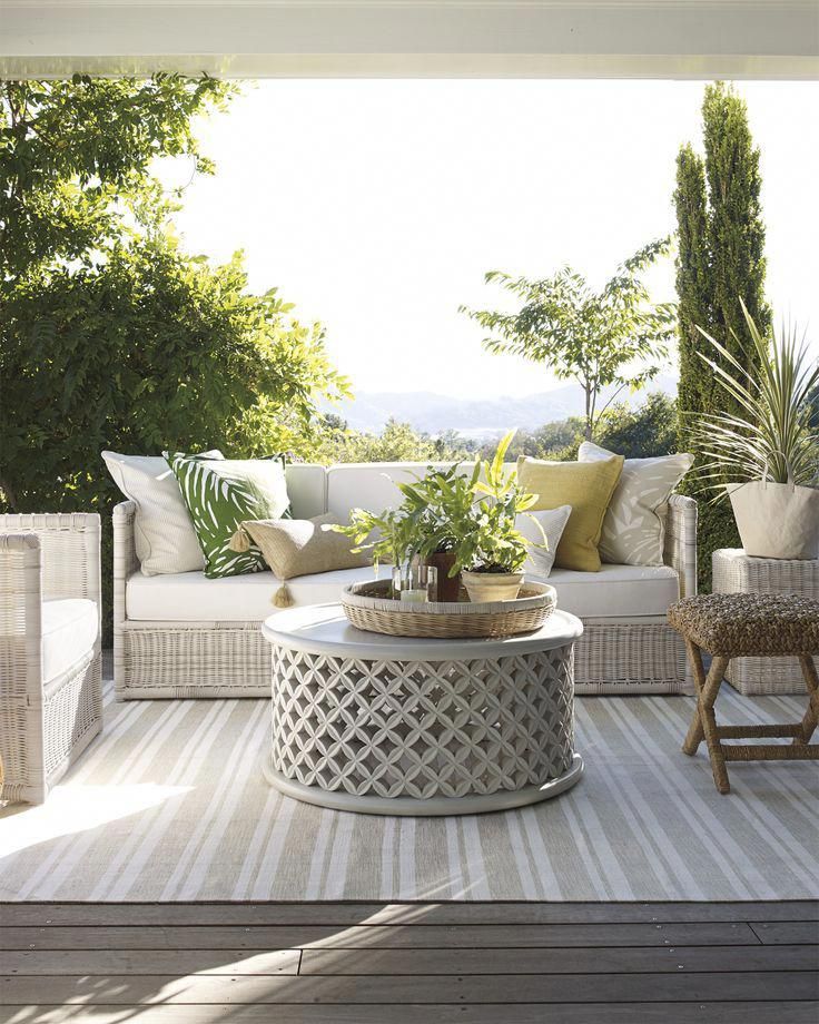 an outdoor living room with white furniture and green plants