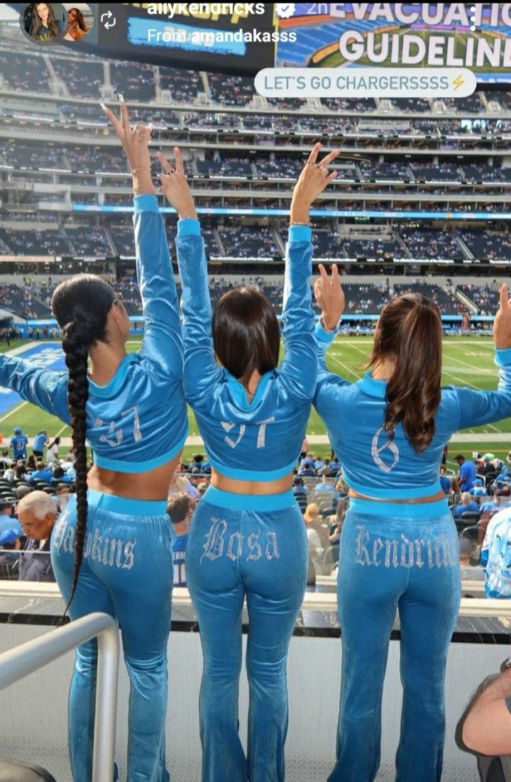 three cheerleaders at a football game in blue outfits with their arms up and hands raised