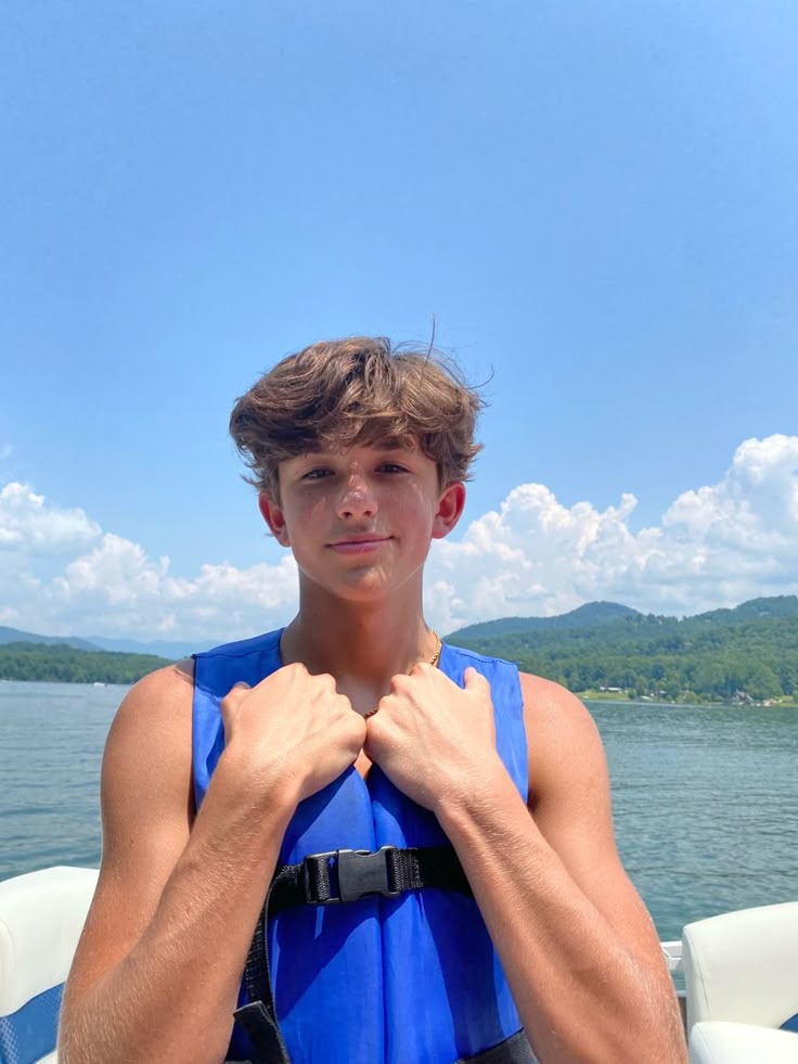 a young man standing on top of a boat wearing a life jacket and holding his hands together