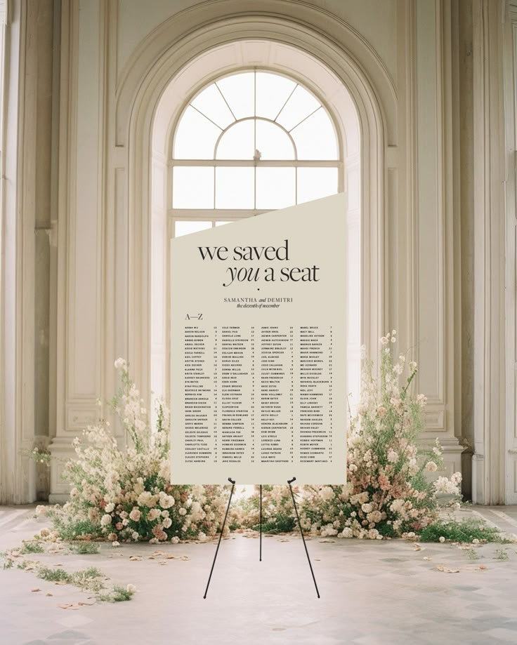 a wedding seating chart with flowers and greenery in front of an arched window on the floor