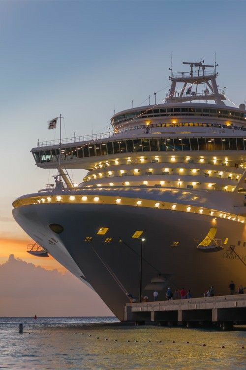 a cruise ship docked in the ocean at dusk with people on it's deck