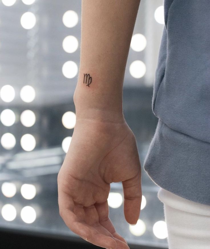 a woman's hand with a small tattoo on her left wrist and the letter m in cursive writing