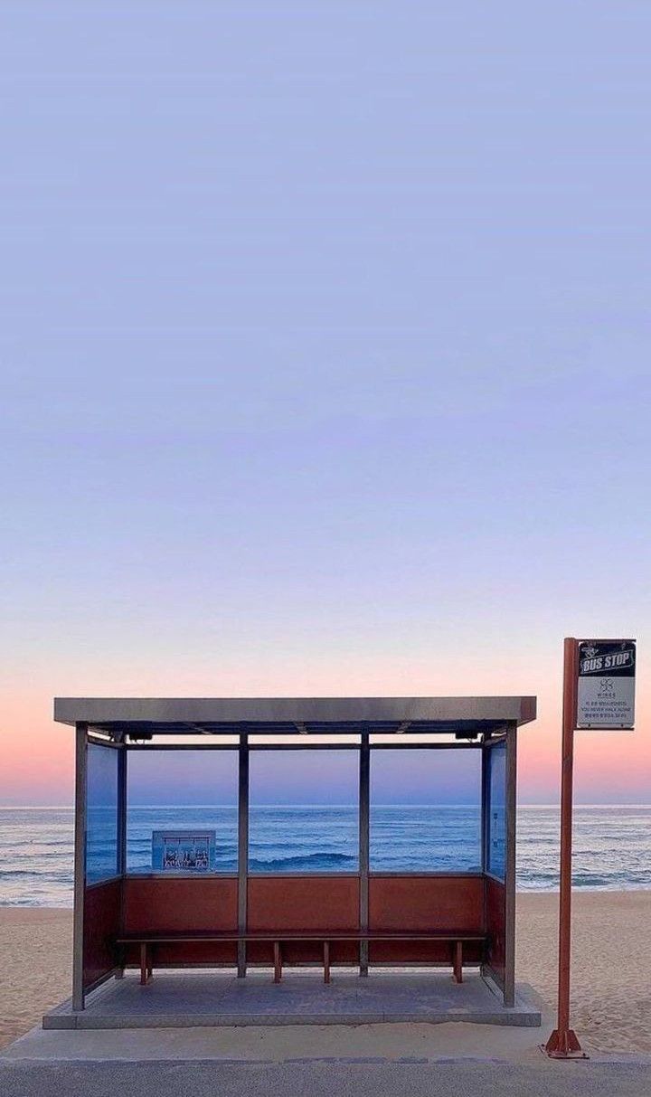 a bus stop sitting on the side of a beach next to the ocean at sunset