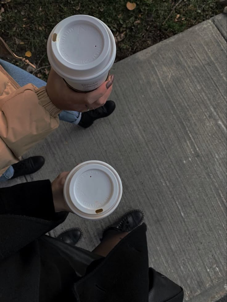 two people standing on the sidewalk with cups in their hands