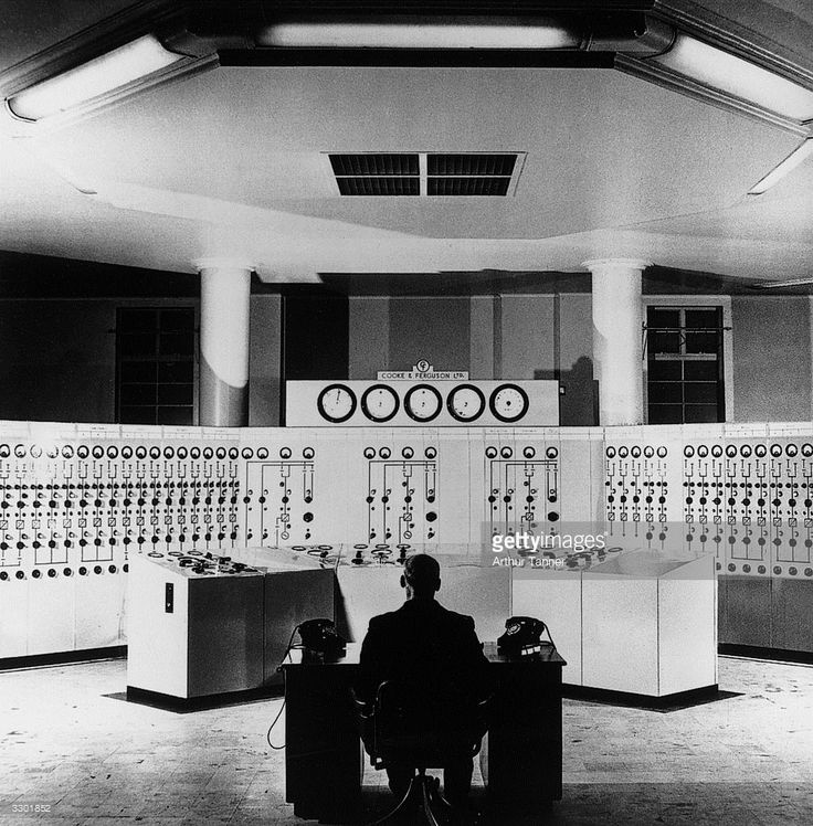 a man sitting at a desk in front of some control boards with buttons on them