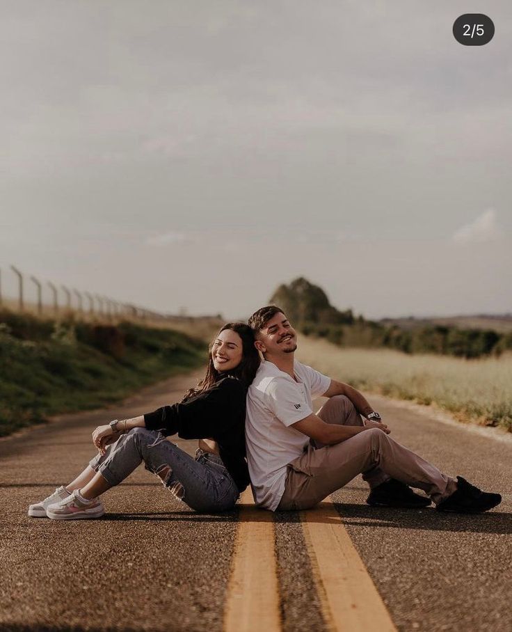 a man and woman sitting on the side of an empty road with their arms around each other