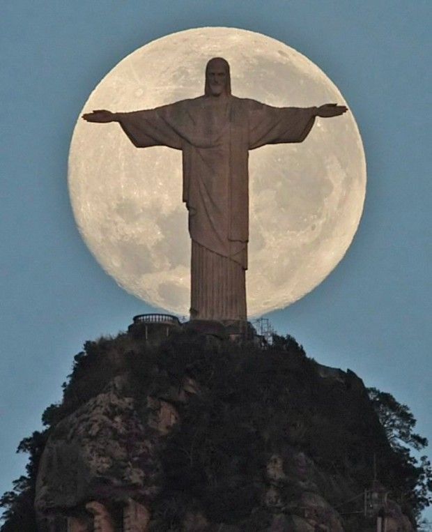 the statue of jesus is on top of a hill with a full moon in the background