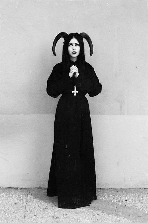 a woman dressed in devilish clothing standing next to a wall with horns on her head