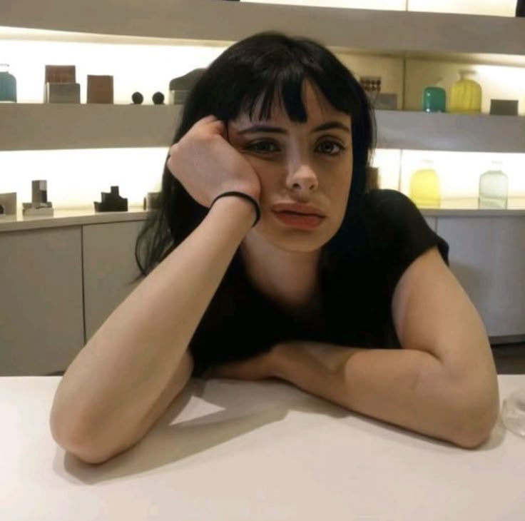 a woman sitting at a table with her hands on her head and looking into the camera