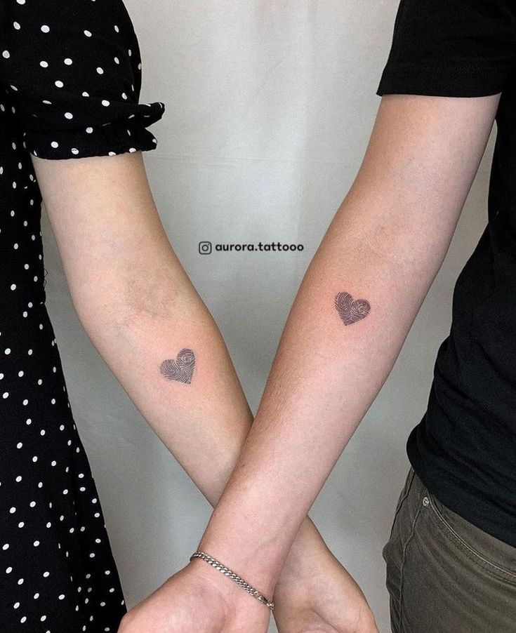 two people holding hands with small tattoos on their arms and hearts tattooed on the wrist