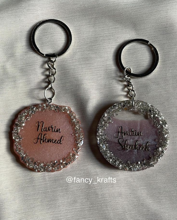 two keychains with the names of two people on them, one in pink and one in silver