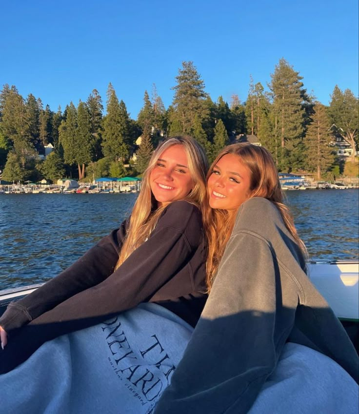 two beautiful young women sitting on the back of a boat in front of a lake