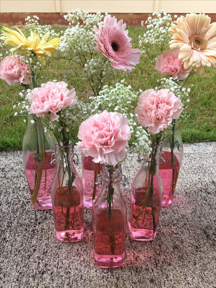 pink and yellow flowers are in glass vases on the ground with grass behind them