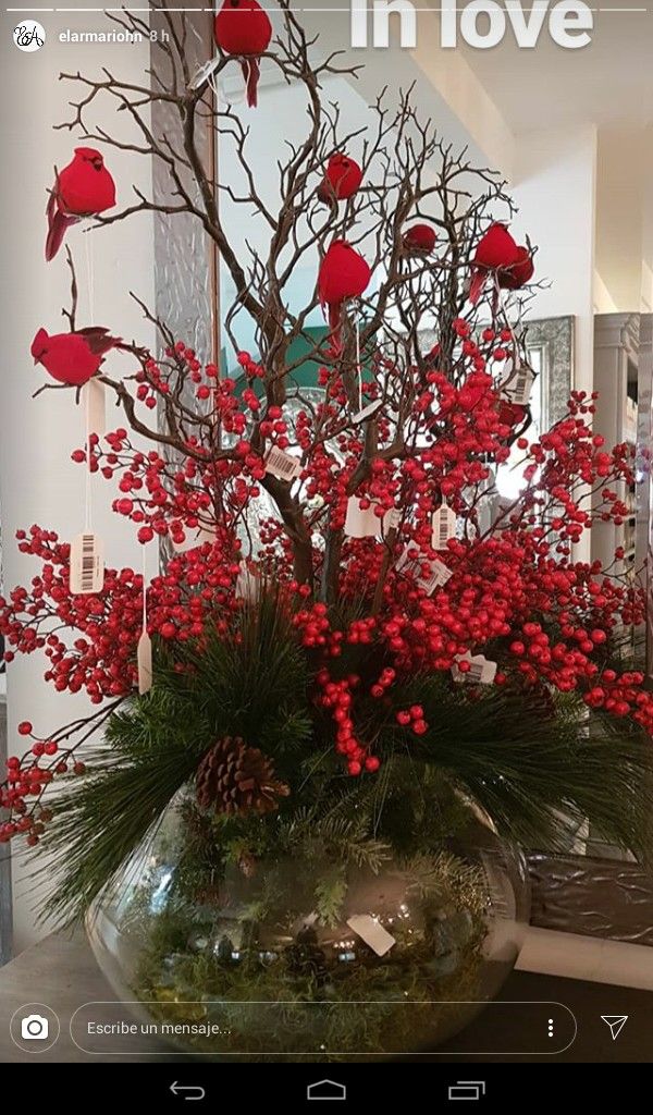 a vase filled with red flowers and berries on top of a table next to a mirror