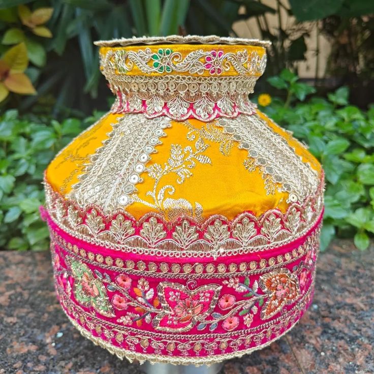 a yellow vase with red and pink trimmings sitting on top of a rock