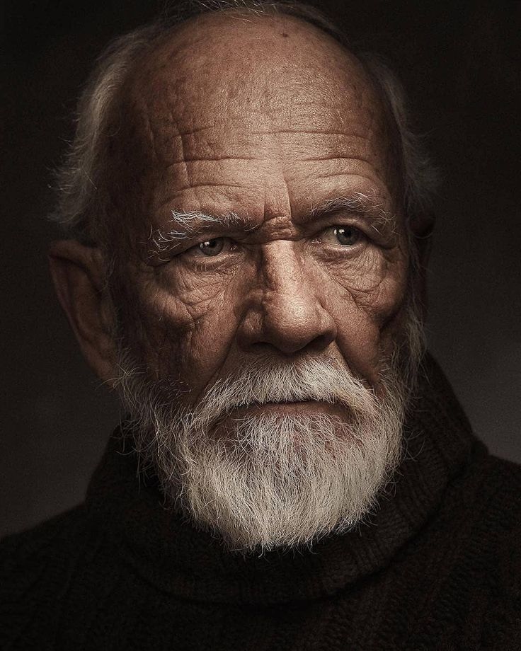 an old man with white hair and beard wearing a black turtle neck sweater looking at the camera