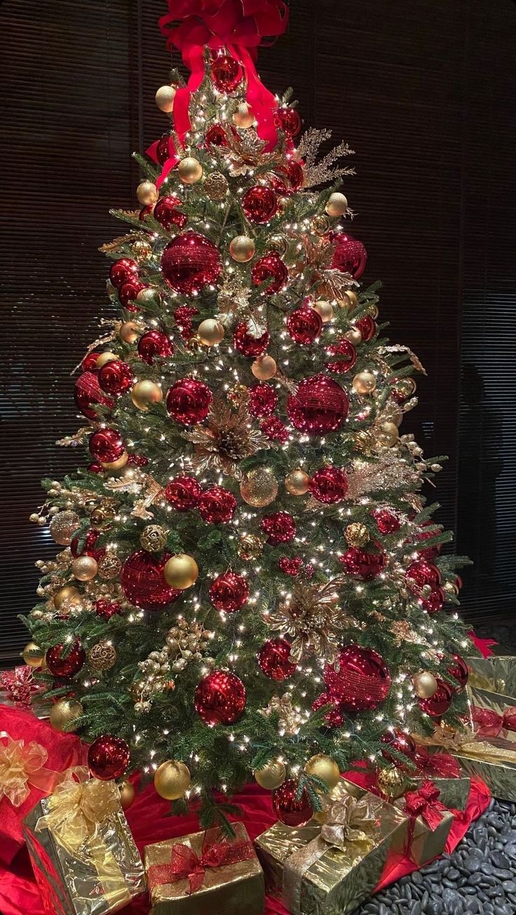 a christmas tree with red and gold ornaments on it's top, surrounded by presents