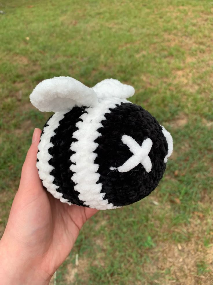 a hand holding a black and white crocheted stuffed animal in front of a grassy field