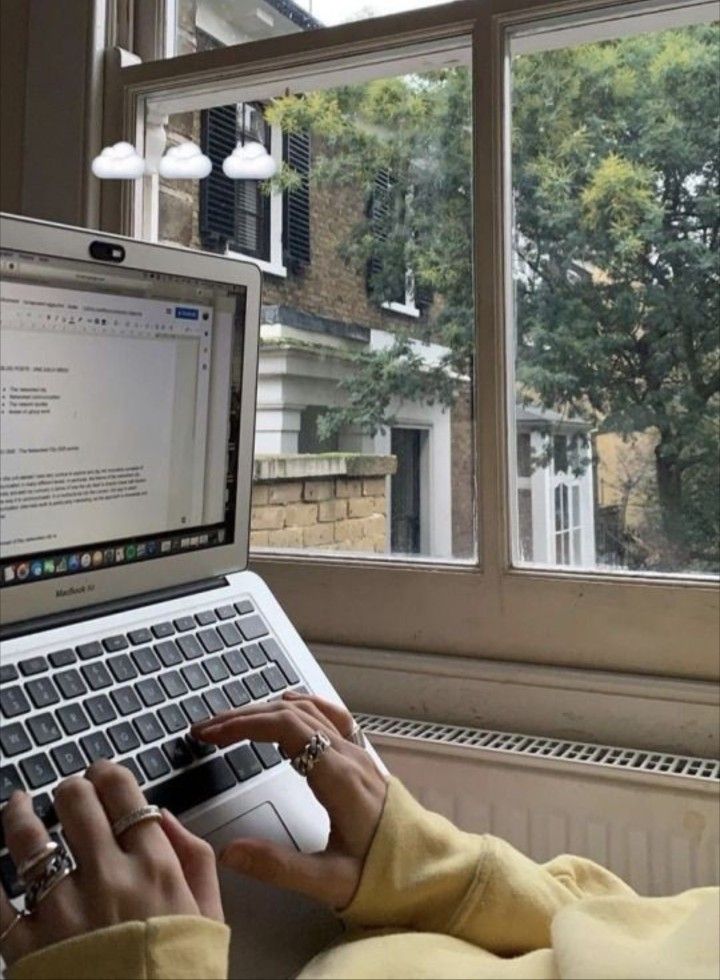 a person typing on a laptop in front of a window