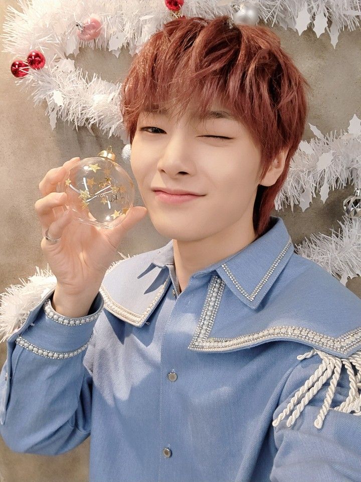 a young man holding a wine glass in front of a christmas tree with white ornaments