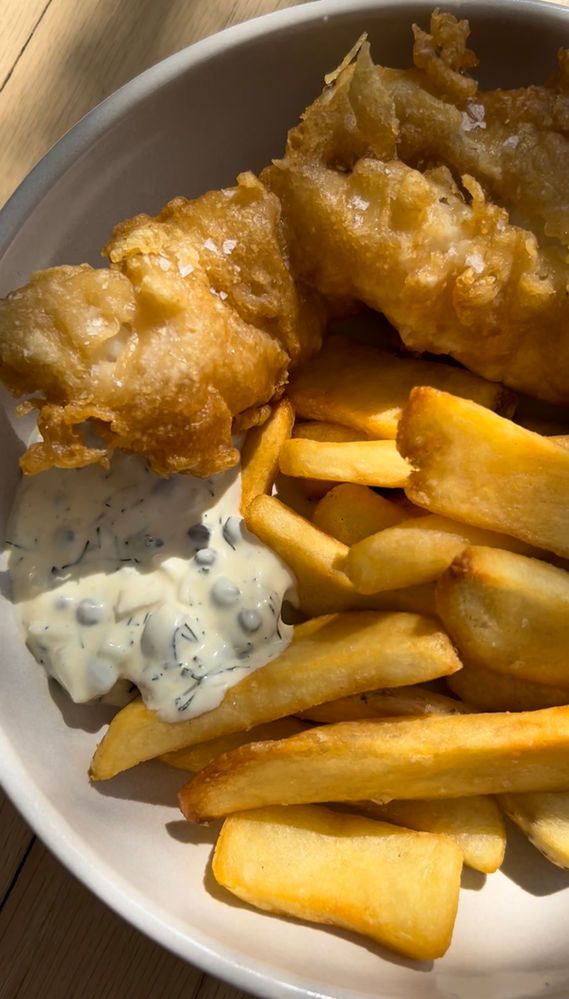 fried fish and fries on a white plate with ranch dressing in the middle, sitting on a wooden table