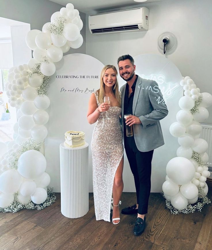 a man and woman standing next to each other in front of a backdrop with balloons