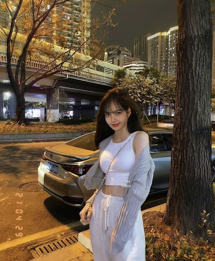 a woman standing next to a tree in front of a car on a city street