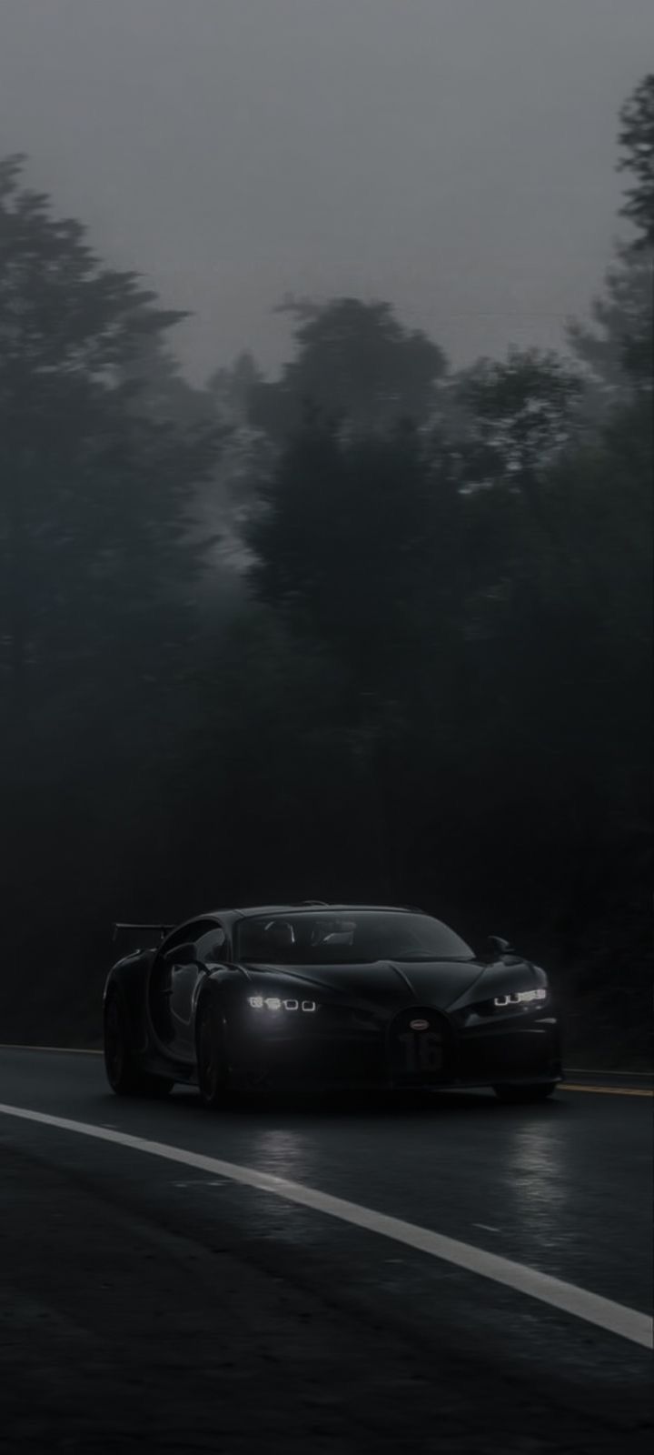 a black sports car driving on a wet road in the dark with trees behind it