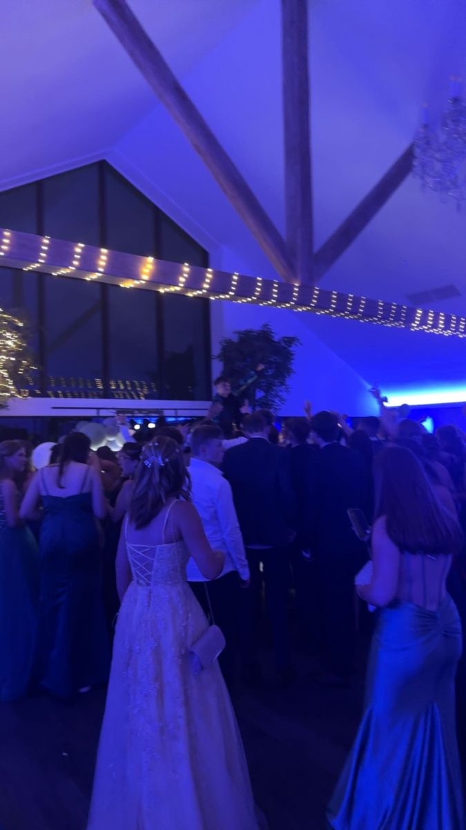 a group of people standing around each other at a formal event with lights on the ceiling