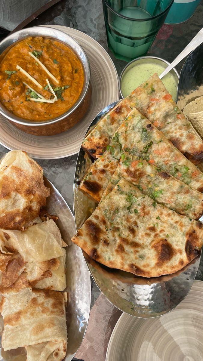 several different types of food sitting on plates and bowls next to each other, including naan bread