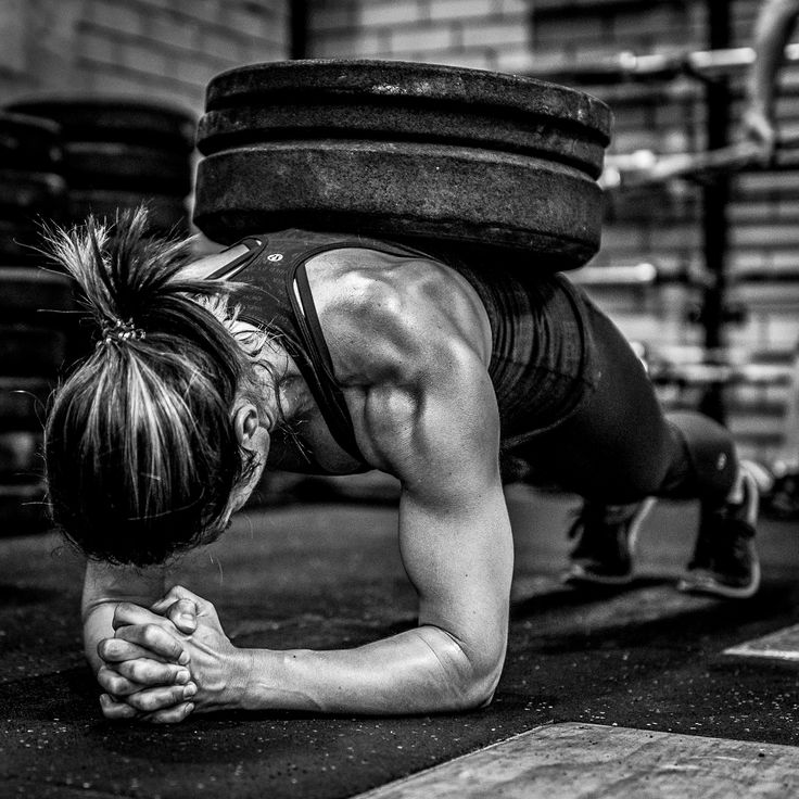 a woman doing push ups with a barbell on her back