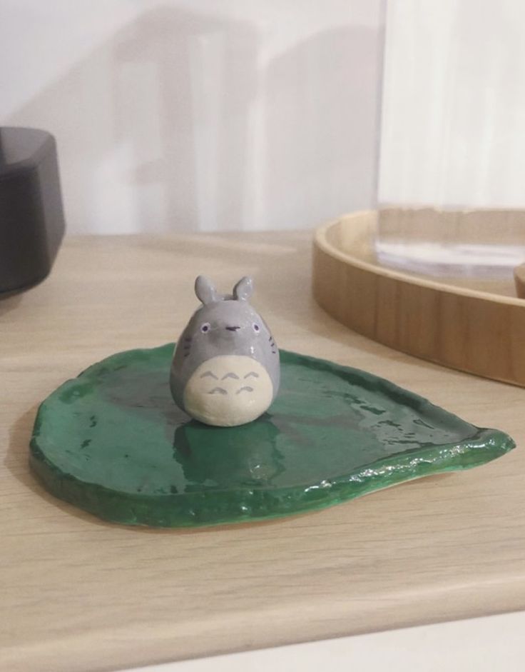 a small ceramic animal sitting on top of a green piece of pottery next to a wooden tray