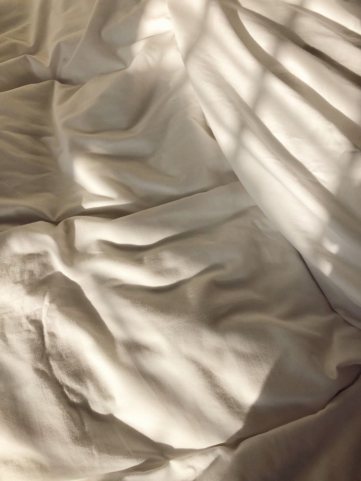 an unmade bed with white sheets and shadows on the sheeted bedspread