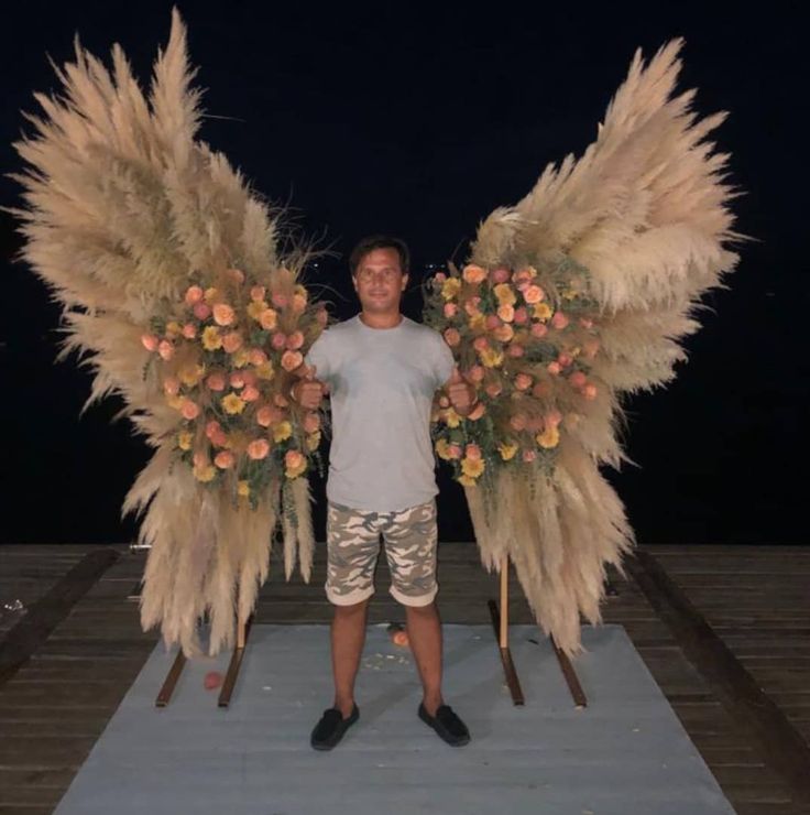 a man standing in front of two large angel wings with flowers on each side and another one behind him