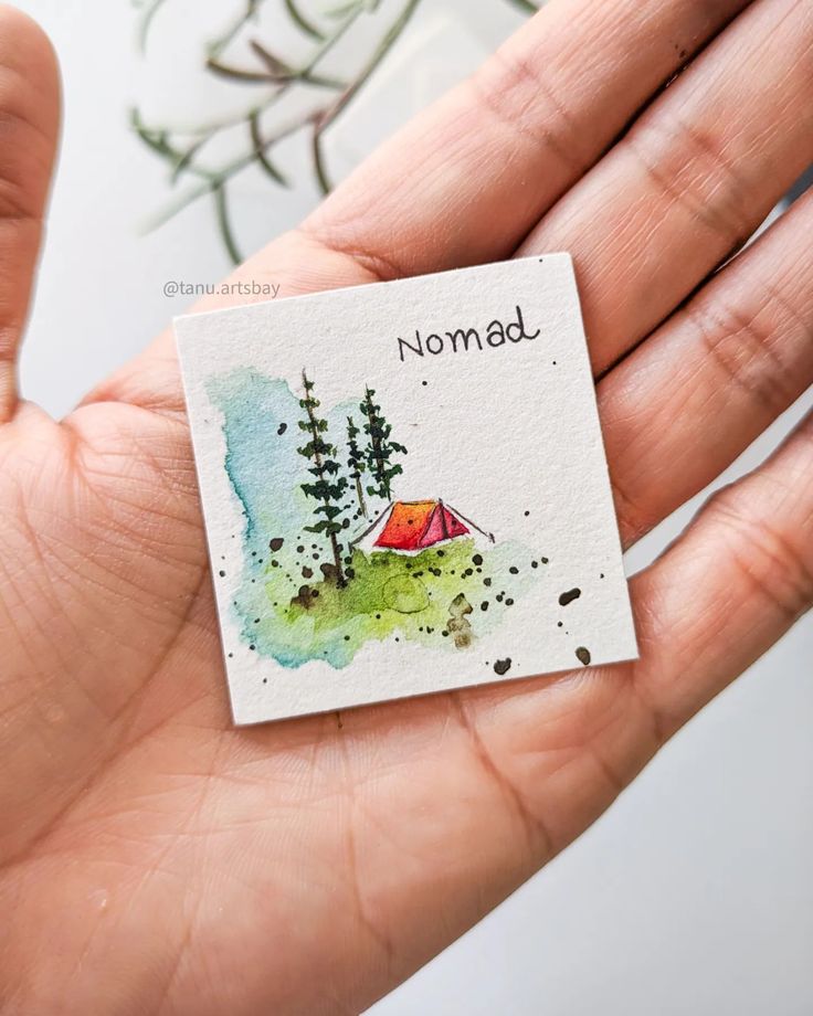 a hand holding a piece of paper with a camper and trees on it that says nomad