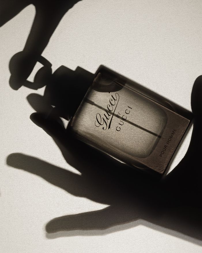 a bottle of perfume sitting on top of a white table next to someone's shadow