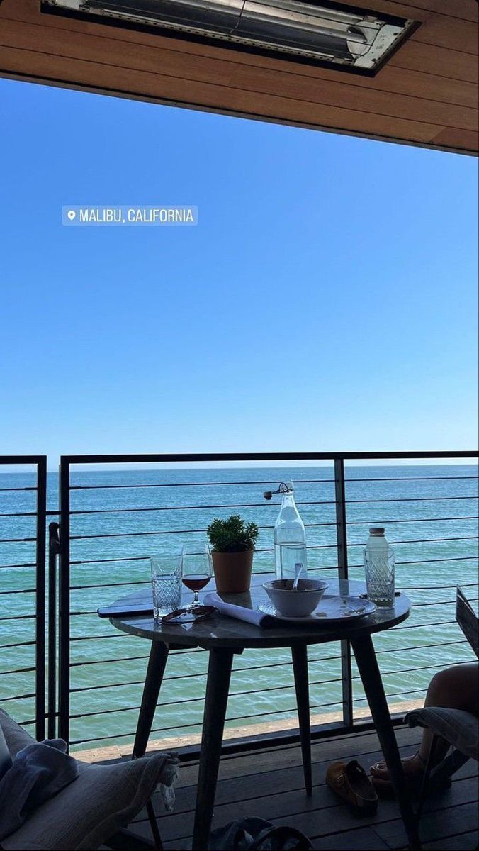 two people sitting at a table on a balcony overlooking the ocean