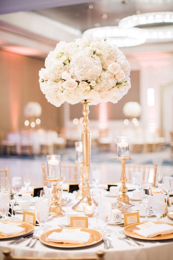 an elegant centerpiece with white flowers and gold accents sits atop a round dining table